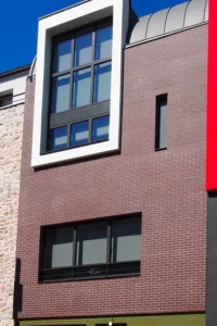 Façade contemporaine de maison de ville en briques, encadrement blanc en saillie et toiture cintrée en zinc, conçue par Le Quilleuc Architecte dans un contexte urbain dense.