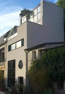 Maison de ville contemporaine avec façade épurée, fenêtres horizontales, hublot et terrasse en toiture, intégrée dans un tissu urbain dense, signée Le Quilleuc Architecte.