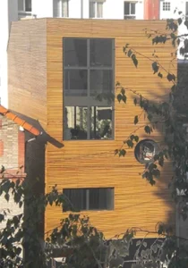 Maison de ville en cœur d’îlot avec façade en bois, grandes ouvertures verticales et hublot circulaire, architecture contemporaine signée Le Quilleuc Architecte.